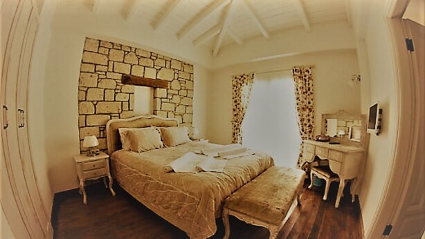 Un dormitorio con pared de piedra, una cama con cabecera, una mesita de noche, un aparador y un televisor.
