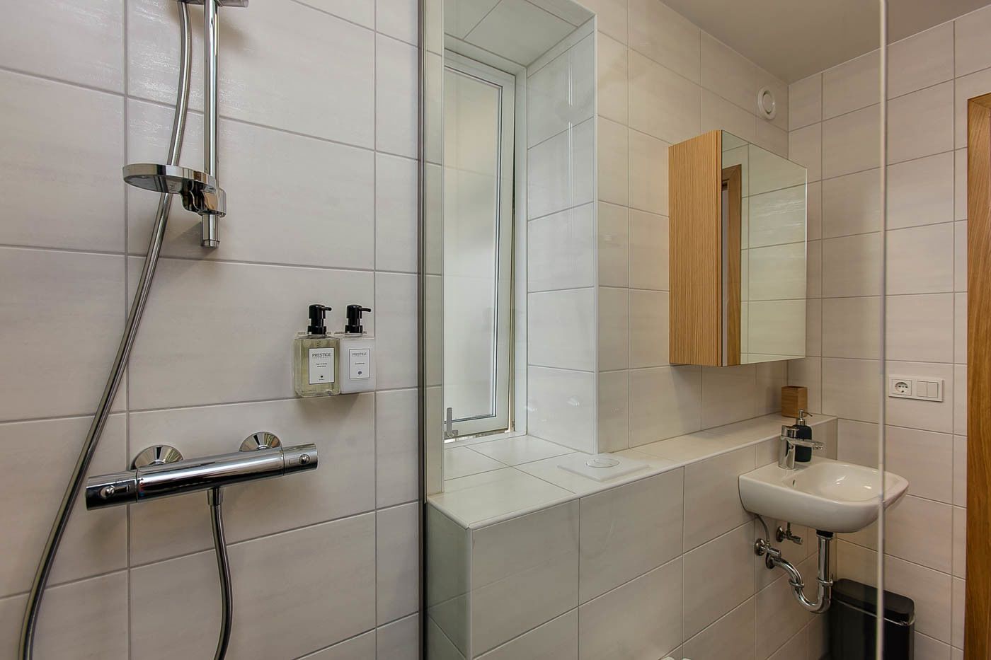 Un baño moderno con cabina de ducha de vidrio, un lavabo blanco y un mueble de tocador de madera.
