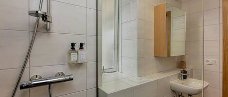 Un baño moderno con cabina de ducha de vidrio, un lavabo blanco y un mueble de tocador de madera.