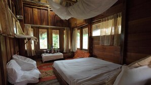 Ein Zimmer mit Holzboden, zwei Betten, einem kleinen Tisch mit Gläsern und einem Fenster mit Vorhängen.
