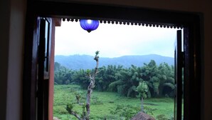 Blick durch eine offene Tür, der einen Blick auf eine üppige grüne Landschaft mit Bäumen und einem fernen Gebirgszug freigibt, mit einer blauen hängenden Leuchte.