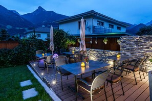 Un patio al aire libre con mesas y sillas, un muro de piedra y montañas al fondo.
