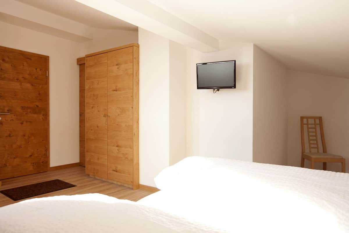 A bedroom with two beds, a wooden wardrobe, a television mounted on the wall, and a chair.