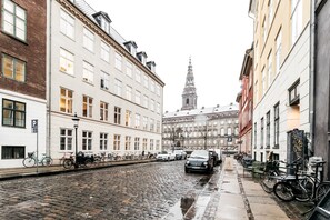 A cobblestone street lined with historic buildings, bicycles, and parked cars.