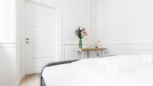 A hotel room with a bed, a bedside table with a vase of flowers, and a white door.