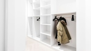 A white closet with multiple shelves and hanging space, featuring a coat with a fur-lined hood.