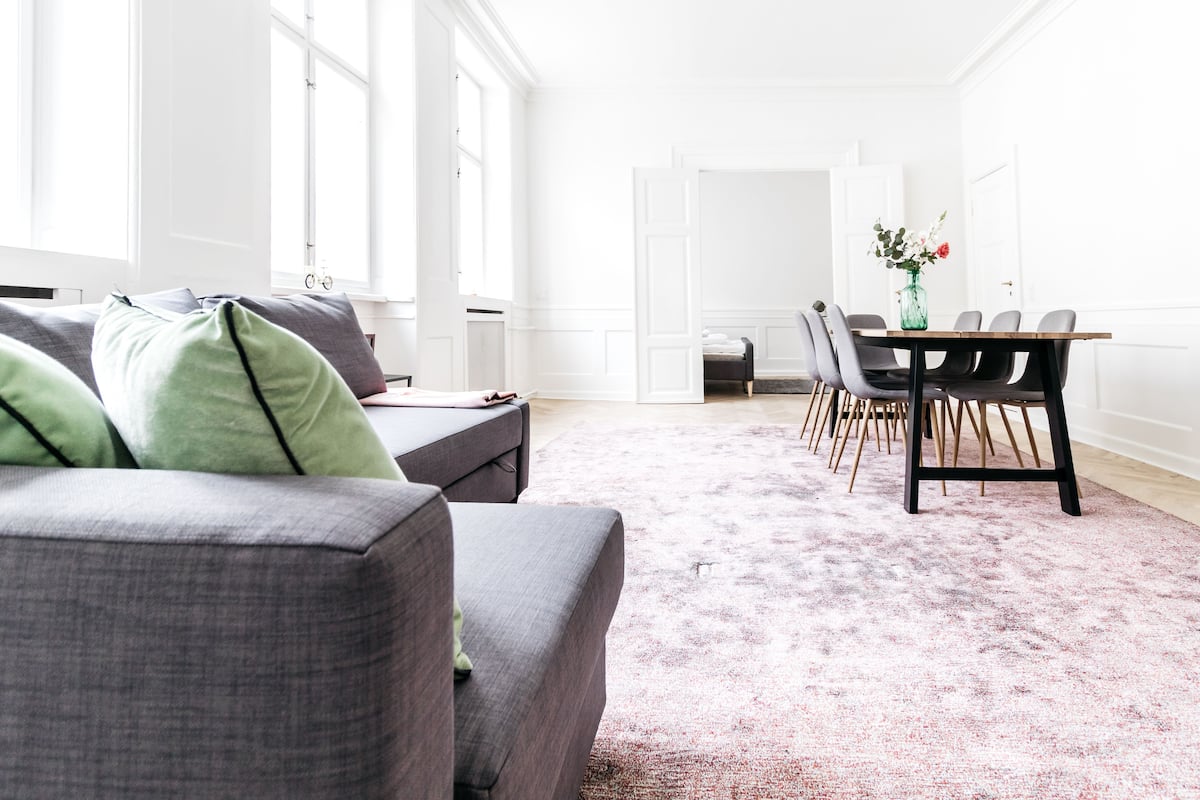 Ein modernes Wohnzimmer mit grauem Sofa, einem Esstisch mit Stühlen und einem großen Fenster, das für natürliches Licht sorgt.