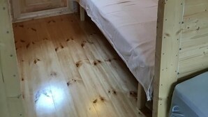 A small, wooden room with a single bed, a door with a window, and a light fixture on the wall. - Framtid Camping Lodging Barrels (Djupivogur)