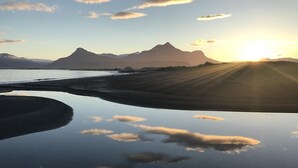 A reflective water surface with mountains in the background and the sun setting or rising. - Framtid Camping Lodging Barrels (Djupivogur)