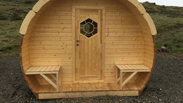 A wooden sauna with a hexagonal window, two benches, and a door. - Framtid Camping Lodging Barrels (Djupivogur)