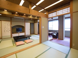 A traditional Japanese room with tatami flooring, a low table with cushions, a television, and sliding doors leading to another room. - Ikaho Grand Hotel (Shibukawa)