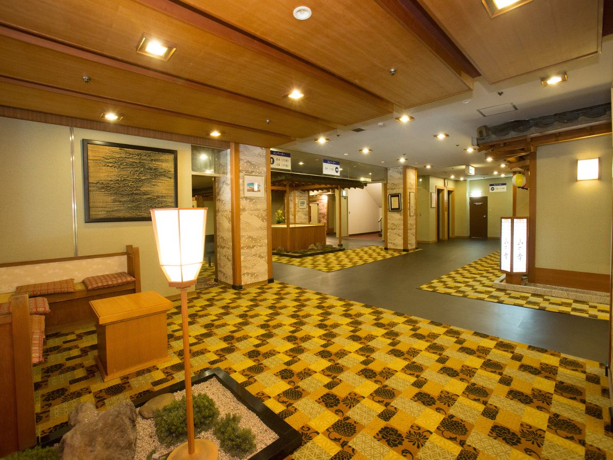 Un vestíbulo de hotel con suelo a cuadros, bancos de madera, un mostrador de recepción y un farol tradicional japonés.
