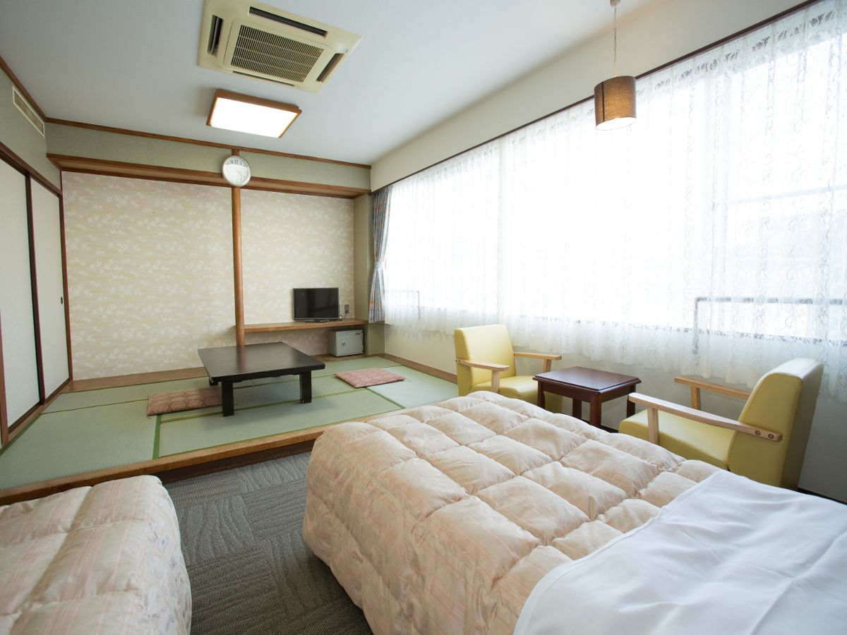 A hotel room with a bed, a desk, a chair, a television, and a futon.