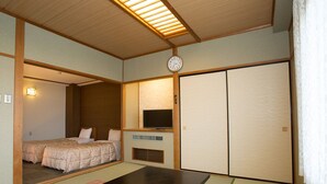 Ein traditioneller japanischer Raum mit Tatami-Böden, einem niedrigen Tisch, einem Fernseher und Schiebetüren.