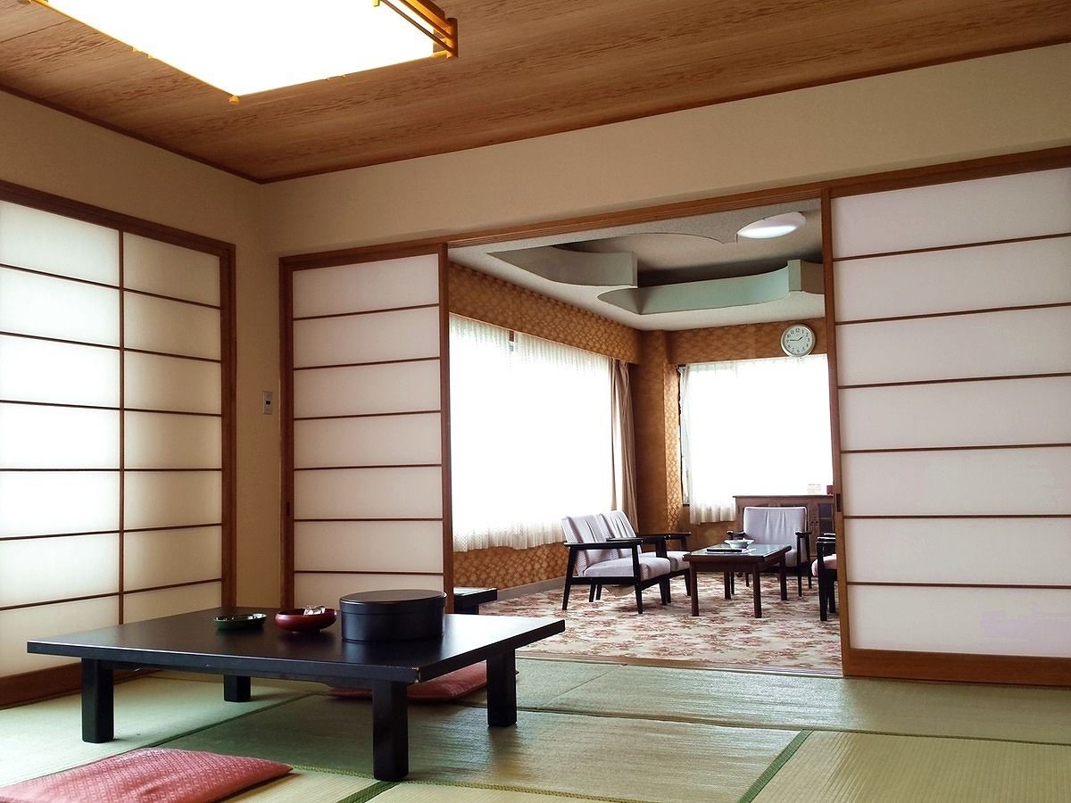 Une pièce de style japonais traditionnel, avec un sol recouvert de tatamis, une table basse avec des coussins et des portes coulissantes.