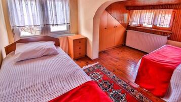 A bedroom with two beds, a window with curtains, a radiator, and a wooden ceiling.