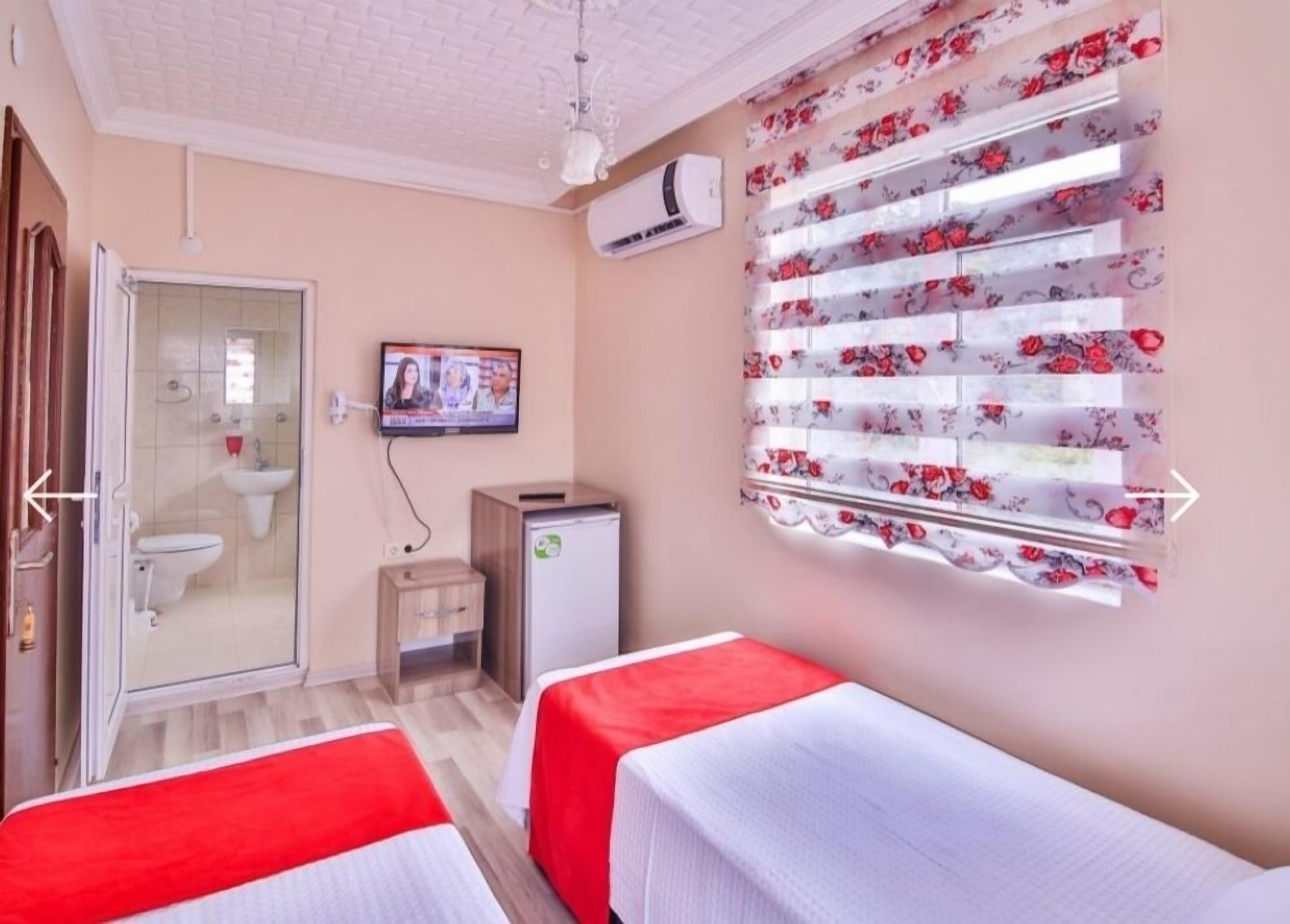 Habitación de hotel con dos camas, televisión, aire acondicionado, ducha y ventana con persianas florales.