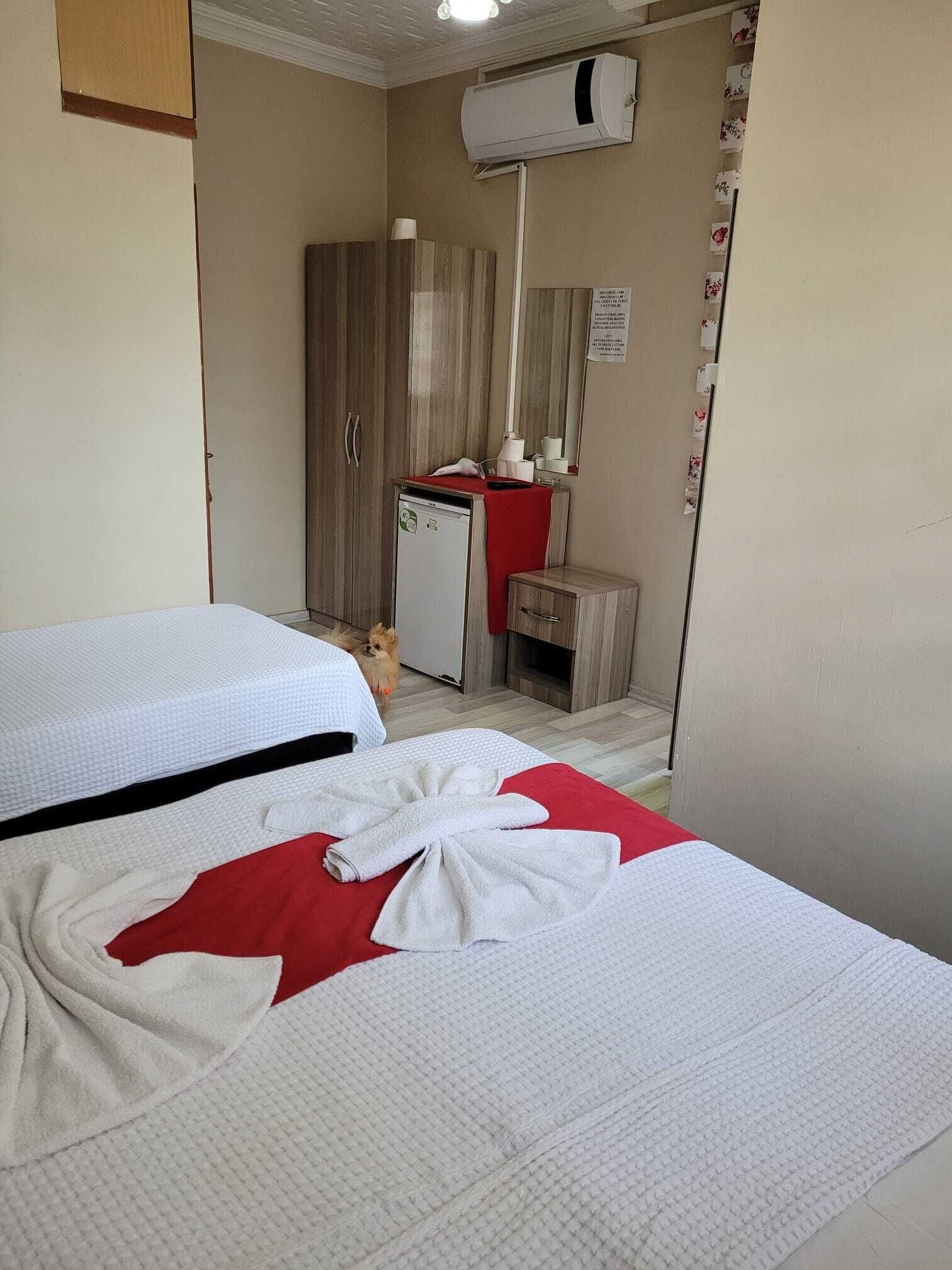 A hotel room with two beds, a small kitchenette, a mirror, and a wall-mounted air conditioner.