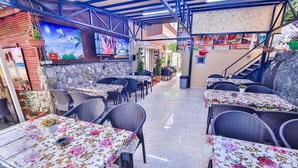 Un restaurante con terraza, paredes de piedra y un mural. Las mesas están cubiertas con manteles florales.