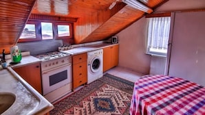 Una cocina compacta con estufa, horno y lavadora, una pequeña mesa con mantel a cuadros y una ventana con cortinas.