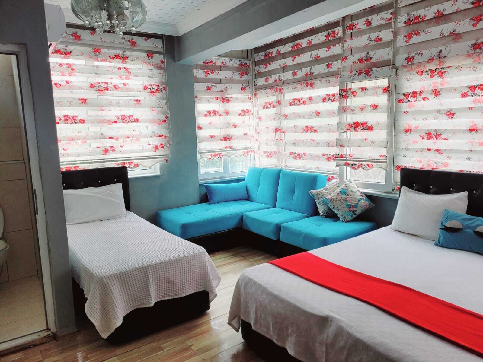 A hotel room with two single beds, a sofa, and a large window with floral curtains.
