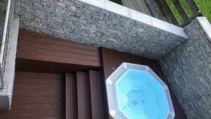 A hot tub on a wooden deck with a stone wall backdrop. - Appartements OLYMPIA (Schwendau)