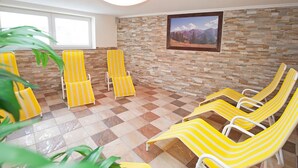 A sunroom with yellow striped lounge chairs, a stone wall, and a framed landscape painting. - Appartements OLYMPIA (Schwendau)