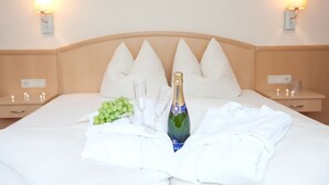 A neatly made bed with a bottle of champagne, glasses, and a bunch of grapes on the bed. - Appartements OLYMPIA (Schwendau)