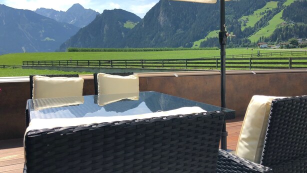 A table and chairs under an umbrella with a mountain view. - Appartements OLYMPIA (Schwendau)
