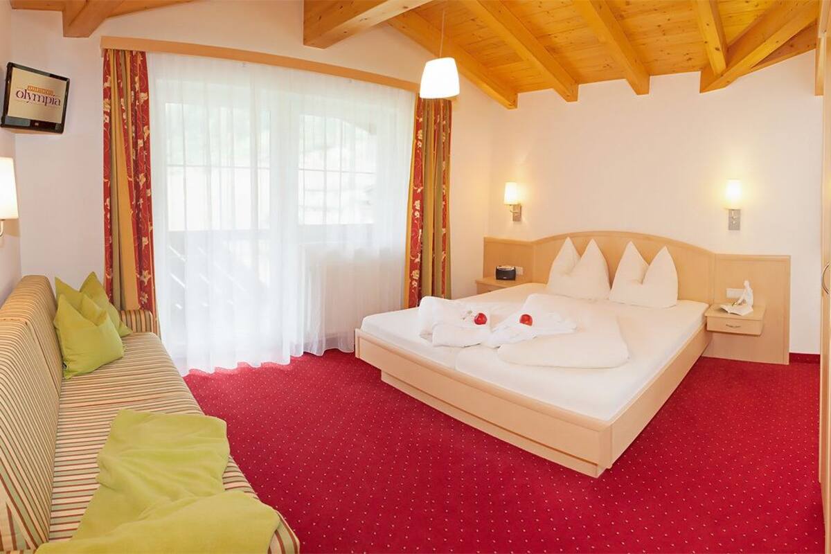 A hotel room with a bed, a sofa, and a window with curtains.