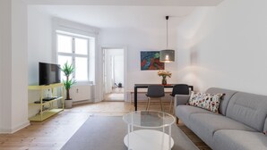 En moderne stue med en grå sofa, et glasbord, en gul underholdningsreol, et spisebord med stole og et stort vindue.