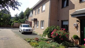 Eine Wohnstraße mit einem weißen Auto, Backsteinhäusern und einem Blumenbeet.