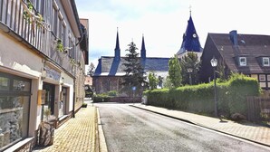 A street with traditional European architecture, including a church with multiple spires and a building with a sign that reads "ALTERNATIVE PERSONAL CARE." - Altstadt Pension Orchidee (Wernigerode)