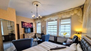 A hotel room with a large bed, two armchairs, a small table, a TV, and a window with curtains. - Altstadt Pension Orchidee (Wernigerode)