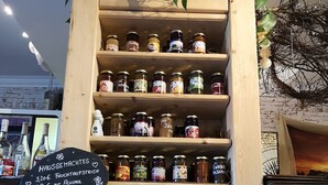 A wooden display shelf with various jars of preserves and a chalkboard sign listing prices. - Altstadt Pension Orchidee (Wernigerode)