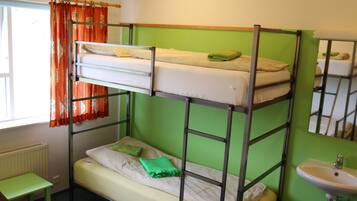 Habitación con literas, una pared verde, una ventana con cortinas naranjas, una mesita y un lavabo.