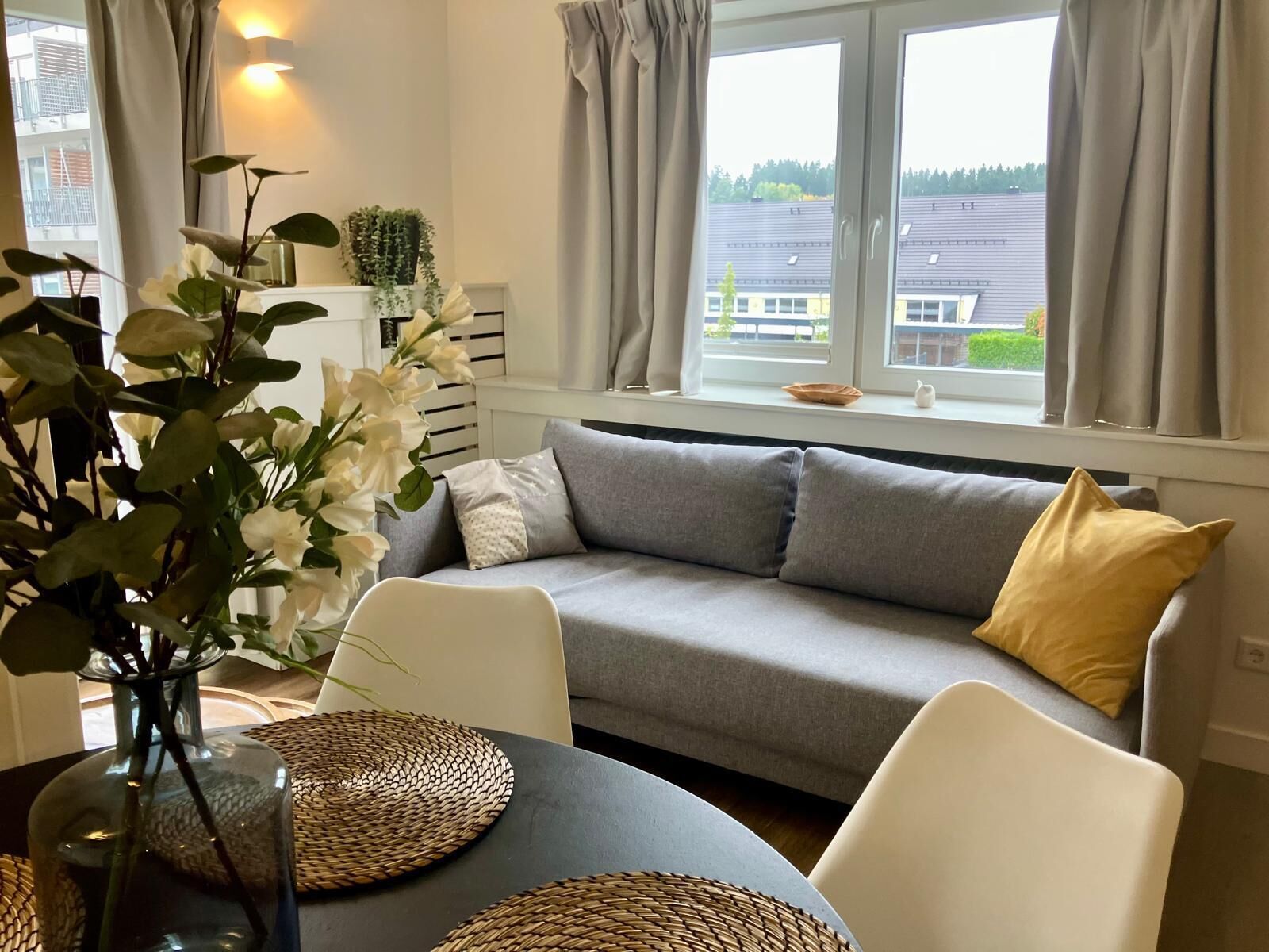 En moderne stue med en grå sofa, hvide stole og et spisebord med vævede servietringe.