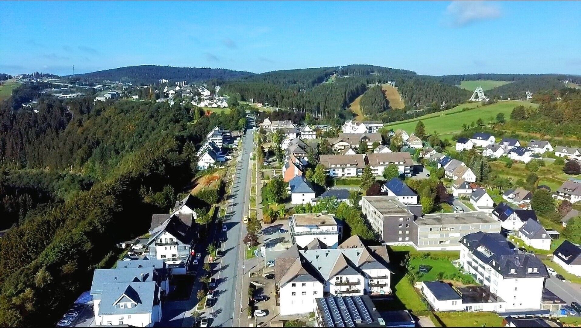 Eine Vogelperspektive eines Wohngebiets mit Häusern, Straßen und einem bewaldeten Hügel im Hintergrund.