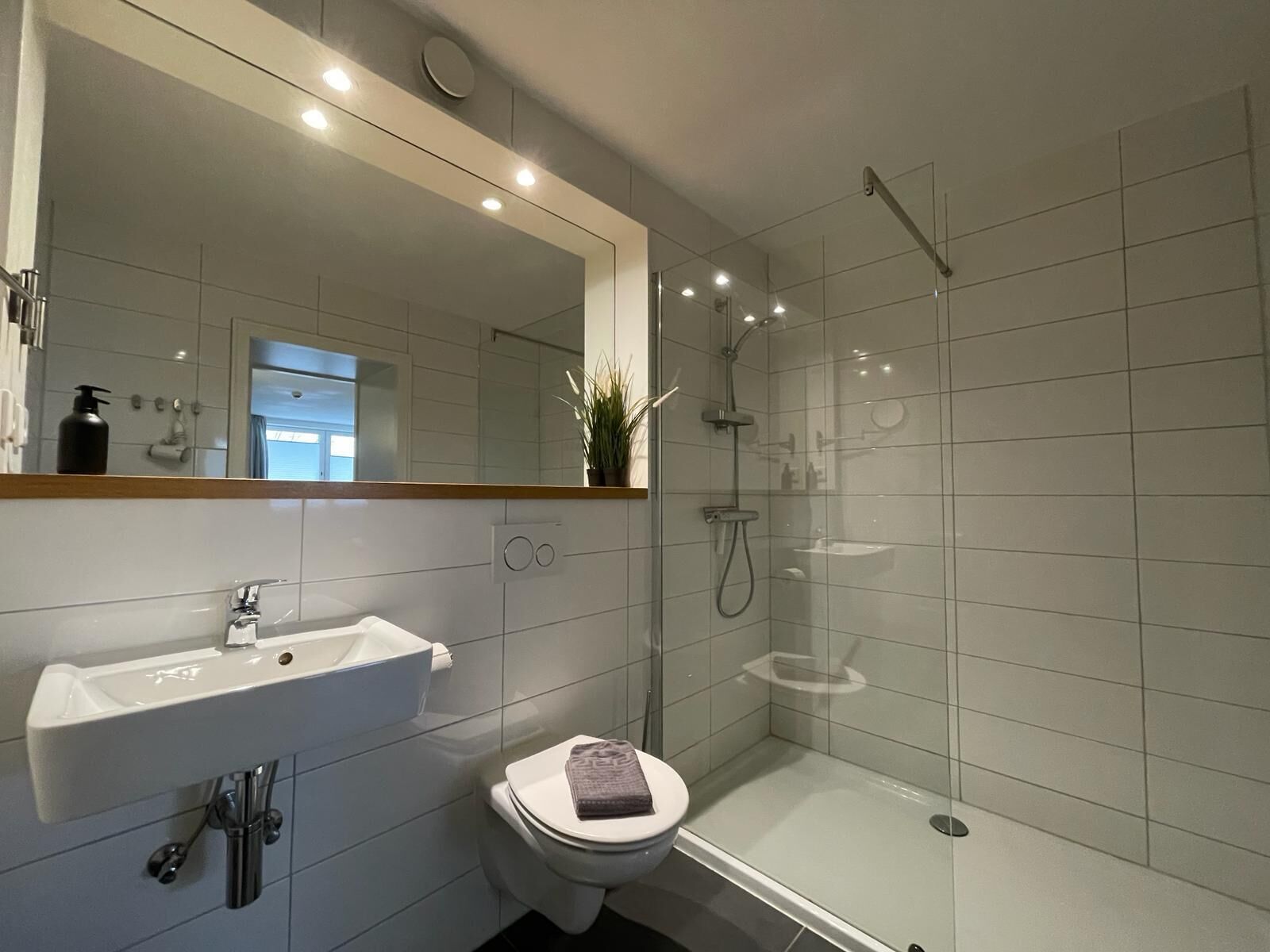 Een moderne badkamer met een witte wastafel, toilet en een douche met glazen wanden.
