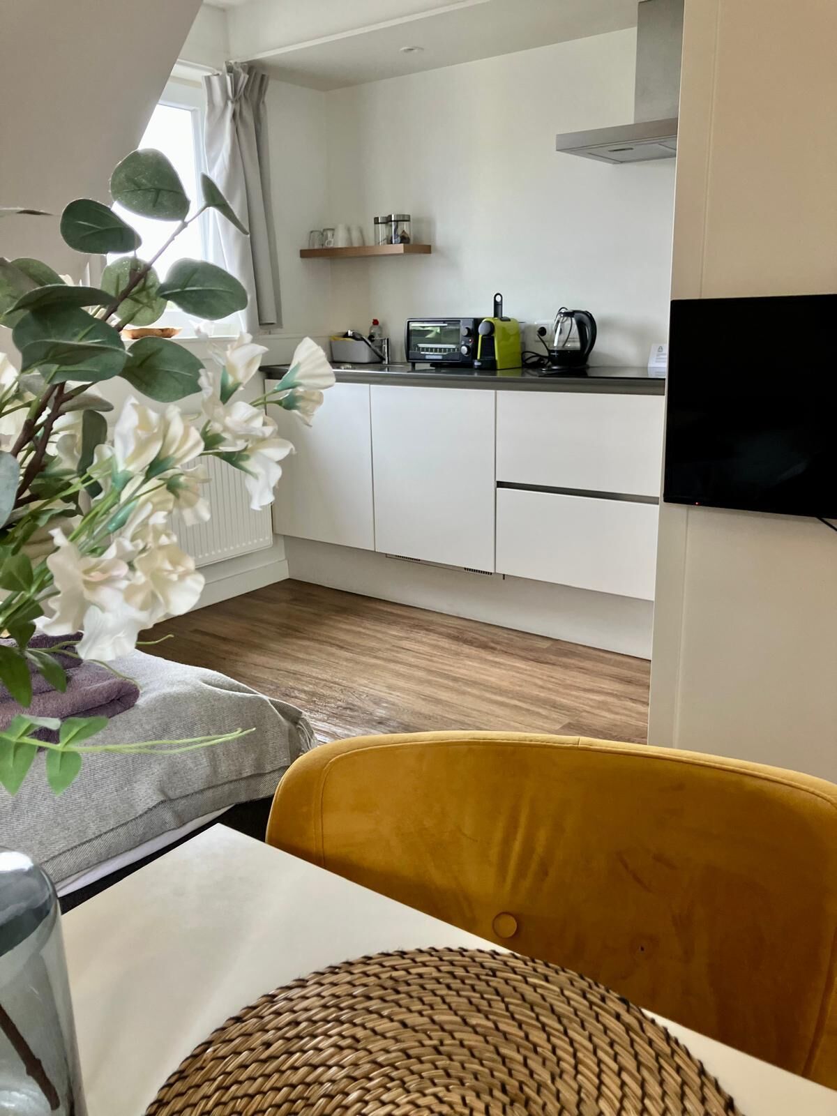 A modern kitchen with white cabinets, a microwave, and a toaster. There is a plant with white flowers on the left.