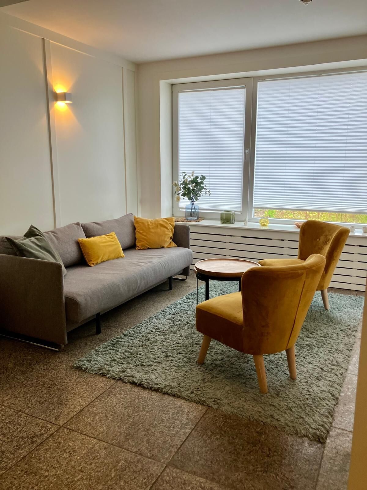 Een moderne woonkamer met een grijze bank, gele kussens, een ronde houten tafel en een geel fauteuil.