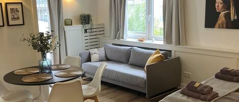 Ein modernes Wohnzimmer mit grauem Sofa, einem Esstisch mit Stühlen und einem Bett mit Handtüchern.