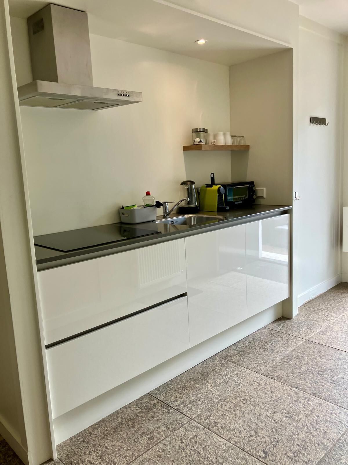 A modern kitchen with white cabinets, a stainless steel range hood, a microwave, and a kettle on the countertop.
