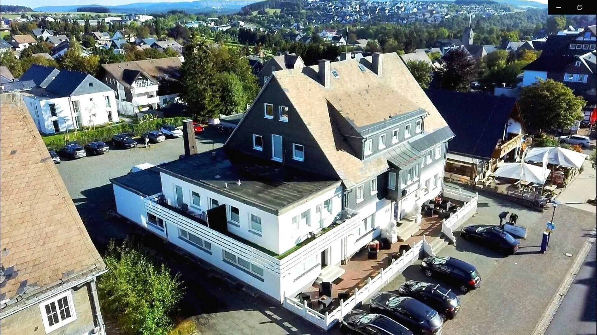 Un bâtiment à deux étages, doté d’un toit à pignon bien visible, d’un porche à l’avant avec des sièges extérieurs et d’un parking où sont stationnées plusieurs voitures.