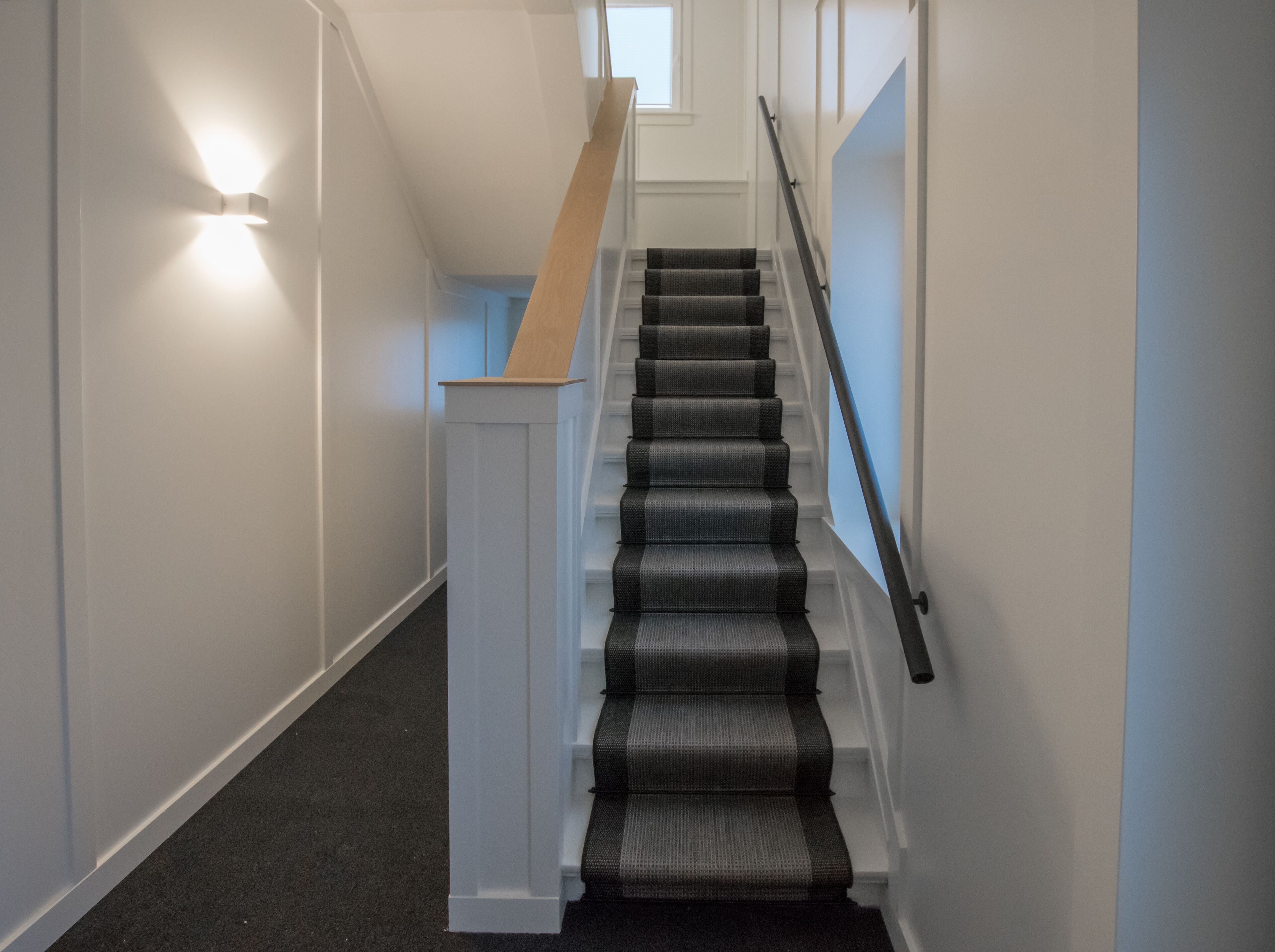Una escalera con barandilla, peldaños alfombrados y una lámpara en la pared.