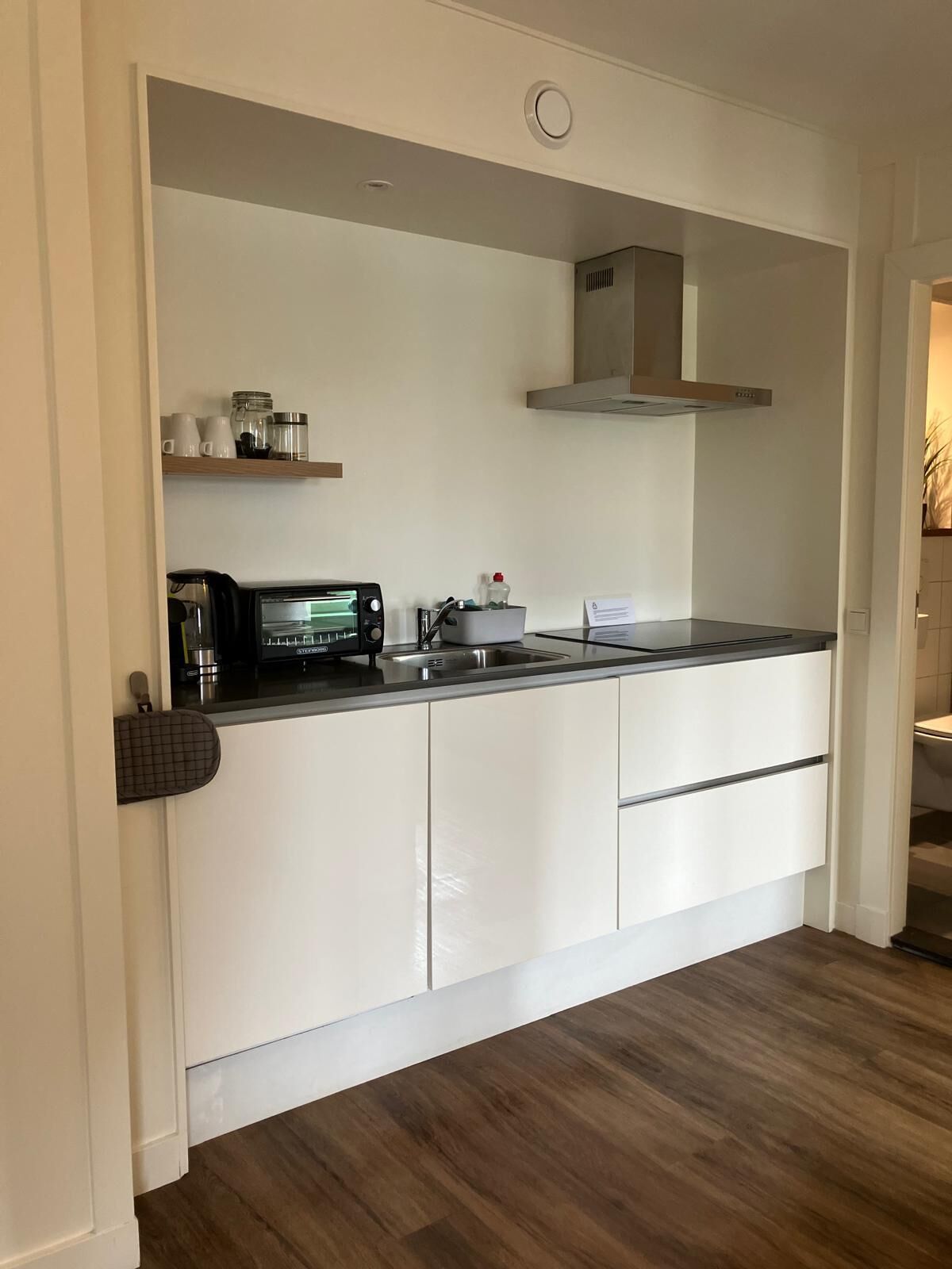 A compact kitchen with white cabinetry, a built-in microwave, and a coffee maker.