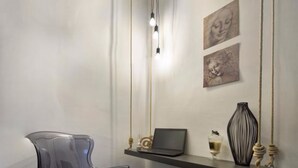 A modern room with a clear plastic chair, a laptop on a floating shelf, and a vase with decorative items. - Suite Vogue Sforza (Voghera)