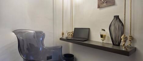 Una habitación moderna con una silla de plástico transparente, una laptop sobre una estantería flotante y un florero con adornos.