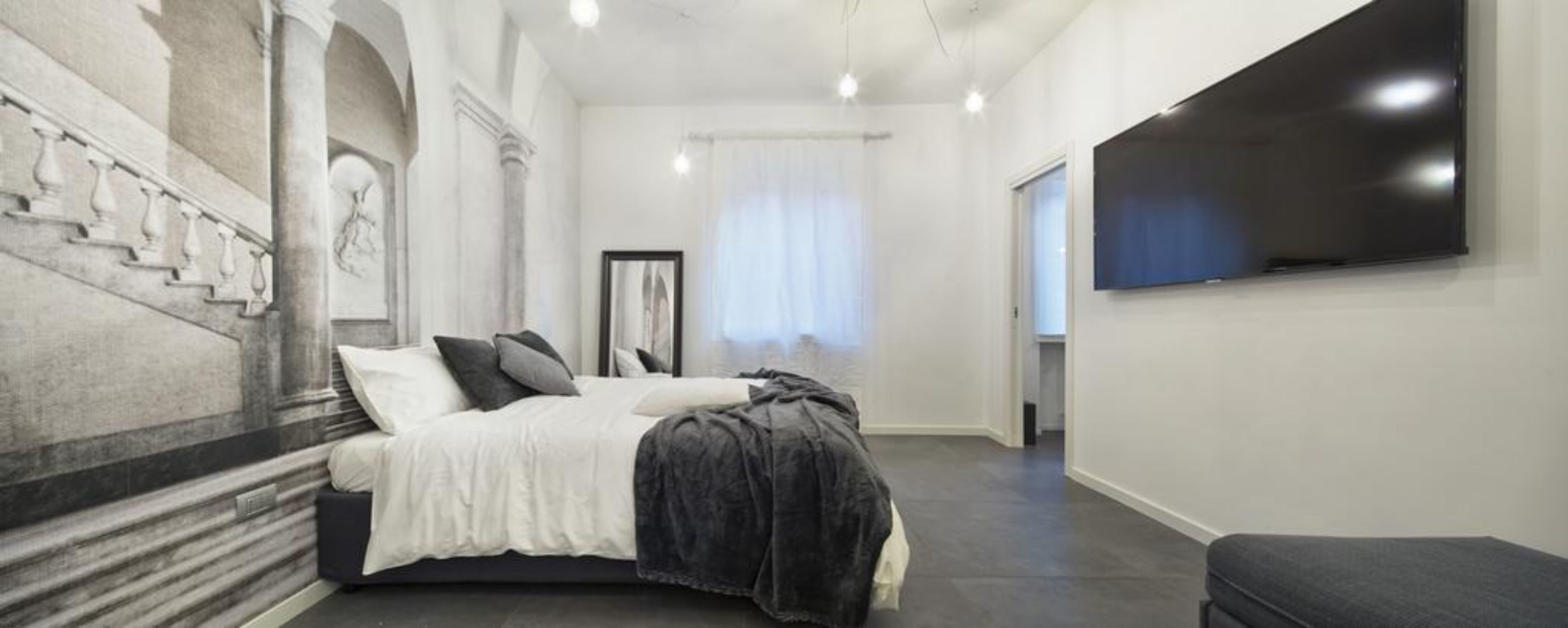 A modern bedroom with a bed, a large flat-screen TV, and a staircase with classical design elements.