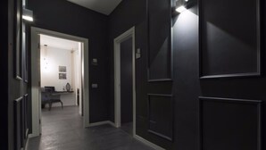 A hallway with dark walls, recessed lighting, and a door leading to a room with a desk and chair. - Suite Vogue Sforza (Voghera)